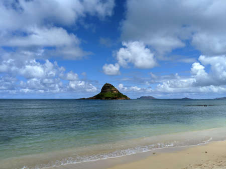 Beach with MokoliÊ»i isalnd or Chinaman's Hat in the distance, which is a 12.5-acre (5.1 ha), 206-foot-tall (63 m) basalt island 1â3 miles (0.54 km) offshore of Kualoa Point, Oahu, in KÄne'ohe Bay, Hawaii.の写真素材