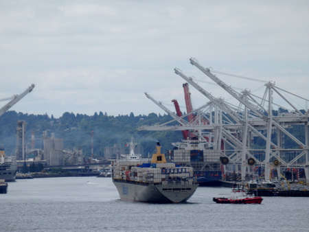 Seattle- June 25, 2016: Matson shipping boat towed out of the Seattle harbor to be unloaded by cranes in as tugboats pushes the boat.のeditorial素材