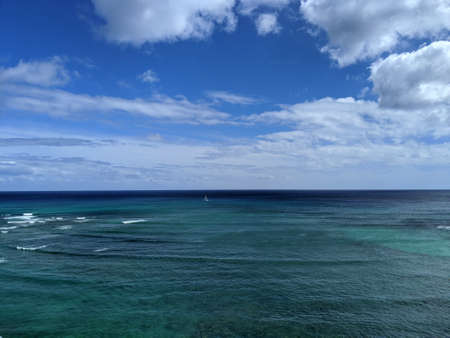 Aerial of Pacific Oeacn with waves rolling in and sail boat in the water and clouds in the sky off Waikiki.の写真素材