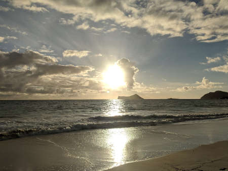 Sunrise over the ocean through the clouds reflecting on Waimanalo Beach with Rabbit and Rock Island in the distance on Oahu, Hawaii.の写真素材
