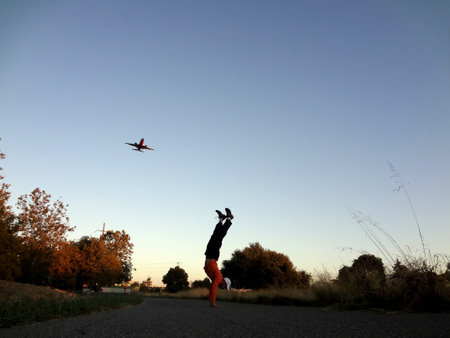 Man does a Handstand with airplane flying in the sky above and trees of a park around him in San Jose, California.の写真素材