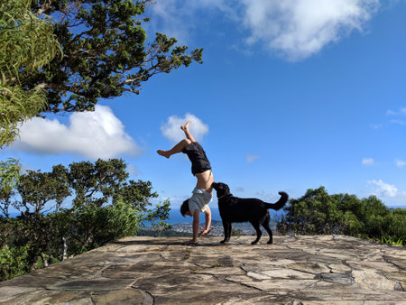 Man wearing a t-shirt, and shorts handstands at Tantalus Mountain with assist from dog with lush...