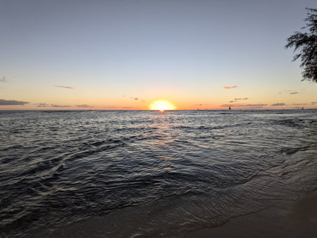 Sunset dropping into the ocean from Waikiki beach with boats sailing on the water on Oahu, Hawaii.の写真素材