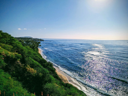 The sun rises over Diamond Head Beach, casting a golden glow over the ocean. The waves crash against the shore. It's a beautiful morning to be at the beach.の写真素材