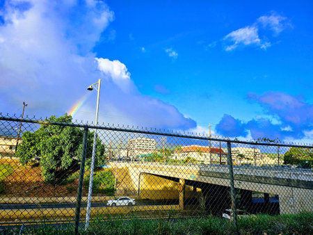 Honolulu - September 17, 2023: Bright rainbow arching over a busy city bridge in Honolulu, Hawaii. Under the bridge, the H-1 highway is visible with cars driving along. The photo captures the contrast between the natural beauty and the urban life in Honolのeditorial素材