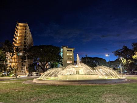 Waikiki - September 19, 2022: Beautifully illuminated fountain in a Kapiolani Park, with a stunning architectural backdrop condos and Elks club.のeditorial素材