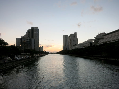 A beautiful photo of a sunset over Ala Wai Canal and the Honolulu skyline, showing the colorful reflections of the sky and the city lights on the water. The photo shows the calm canal, which serves as the northern boundary of the tourist district of Waikiki1. The canal was created in 1928 to drain the rice paddies and swamps which would eventually become Waikiki.の写真素材