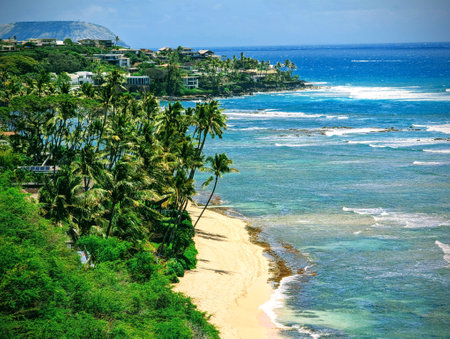 Sandy beach and a blue-green ocean seen from Diamond Head lookout, a high vantage point on the volcanic tuff cone on OÊ»ahu island. The photo shows the white waves crashing onto the shore, the hill with houses and palm trees in the background, and the blue sky with white clouds.の写真素材