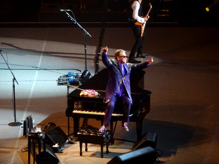 Honolulu - January 10, 2015: Elton John sits on piano with arms in the air on stage with band at the Neal S. Blaisdell Center.のeditorial素材