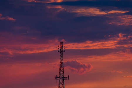 Cell Phone Tower Silhouetted Against Orange and Purple Clouds at Sunsetの写真素材