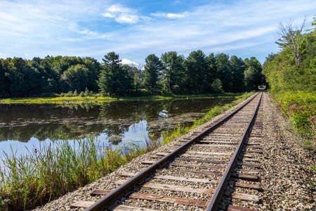 Old abandoned train tracks next to a beautiful pond in the rural countryside stretching off into the distanceの写真素材