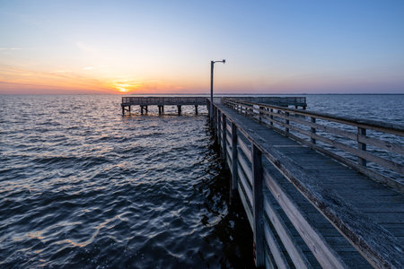 The sun sets over an old, dark, empty, foreboding, wooden pier stretching out over the waterの写真素材