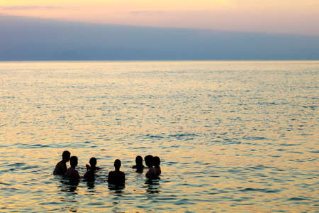 group of people in silhouette alking on the sea at sunset,の写真素材