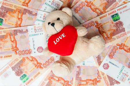 Money. Teddy bear sitting on the money. Money from different countries. Cost concept on white background.の写真素材