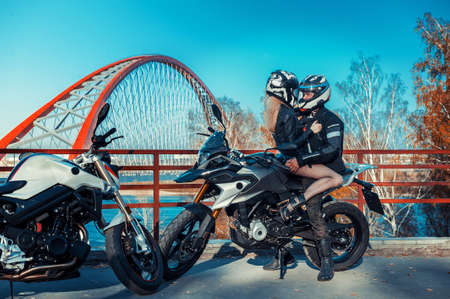 An attractive guy and a young woman in a black leather outfit with a motorcycle.