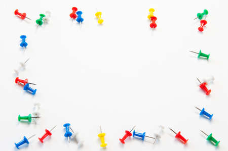multi-colored stationery buttons are randomly stuck into a white sheet of paperの写真素材