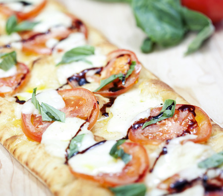 Fresh pizza with tomato, mozzarella and basil on wooden board