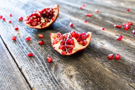 Pomegranate slpit open with the seeds scattered on old wooden planksの写真素材