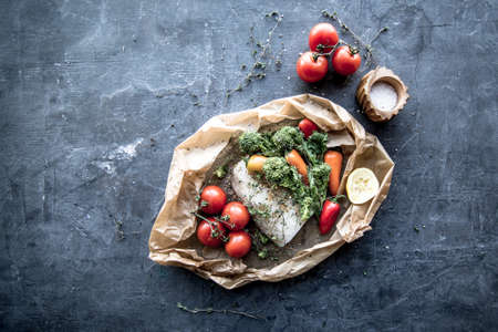 Raw Uncooked Cod on Parchment paper ready for the oven with fresh vegetables.の写真素材