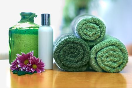 Spa and wellness: green towels, salt and body lotion in bathroom; stones and gerbera decorationの写真素材