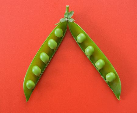 Top view of an open green pea pod on red surface