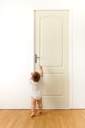 Baby in front of a closed door, trying to reach the keyhole with keyの写真素材