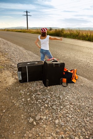 Young hitch-hiker girl standing on road side afternoon with suitcasesの写真素材