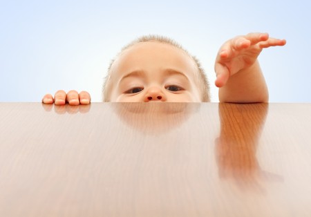 Curious little boy looking up and raising hands onto table surfaceの写真素材