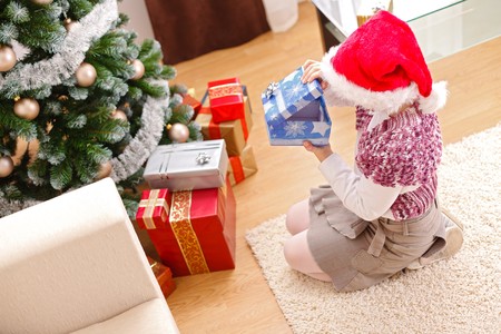 Girl looking inside an empty gift box in front of decorated christmas treeの写真素材