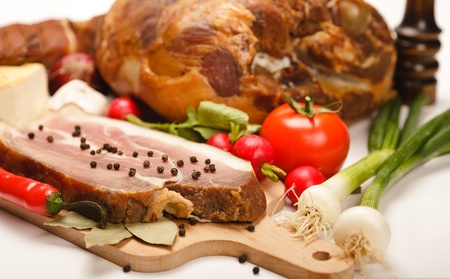 Traditional smoked pork ham slice and whole ham in background. Surrounded with fresh vegetablesの写真素材