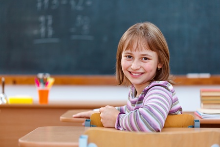 Elementary school girl in classroom, turning back and smilingの写真素材