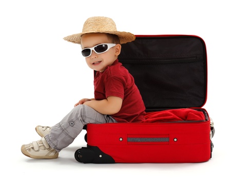 Confident little boy wearing sunglasses and straw hat, sitting in open suitcaseの写真素材
