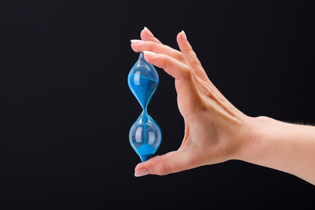 Woman's hand holding sand hourglass on black backgroundの写真素材