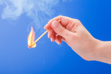Hand holding a burning matchstick on blue background