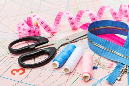 Tailor tools and accessories: scissors, threads, zipper, measuring tap on tailoring pattern