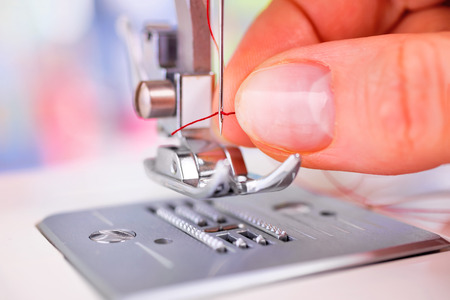 Closeup of woman's hand threading sewing machine needleの写真素材