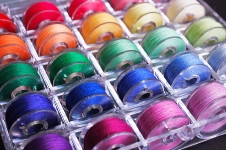 Plastic sewing machine bobbins with colorful threads in storage box