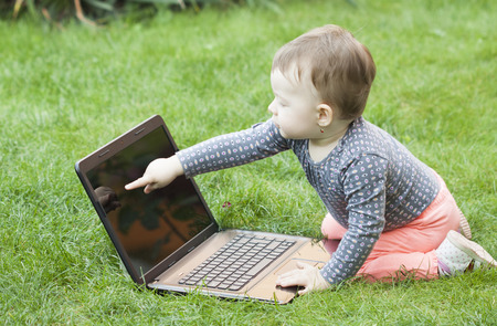 Cute baby girl using a laptop in the gardenの写真素材