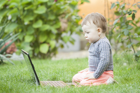 Cute baby girl using a laptop in the gardenの写真素材