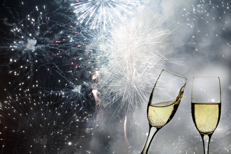 Glasses with champagne against fireworks and holiday lightsの写真素材