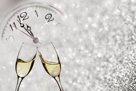 Glasses with champagne against holiday lights and clock close to midnightの写真素材