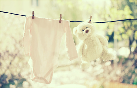 Baby clothes and teddy bear hanging on the clotheslineの写真素材
