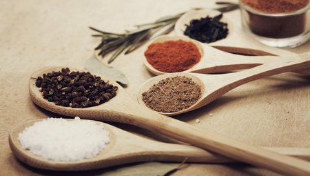Various colorful spices on kitchen spoons over grunge wooden tableの写真素材