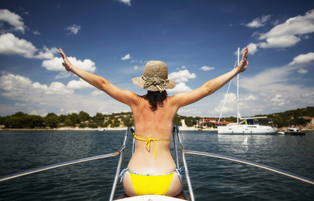 Young woman with hat sitting on the front of a sail boat admiring the view - holiday conceptの写真素材