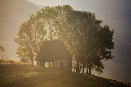 Sunrise in autumn mountains - rural landscape with small cottage in Transylvania, Romaniaの写真素材