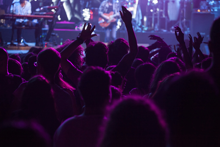 Photo of many people enjoying concert, crowd with raised up hands dancing in nightclub, audience applauding to musician band, night entertainment, music festival.の写真素材