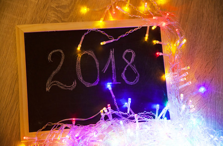 Colorful glowing Christmas lights and 2018 text on small blackboard - New Year concept