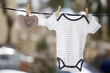 Baby clothes and a brown heart hanging on the clotheslineの写真素材