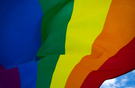 Bright rainbow LGBT flag fluttering against blue sky. LGBT community, happiness, freedom and love concept for same sex couples.の写真素材
