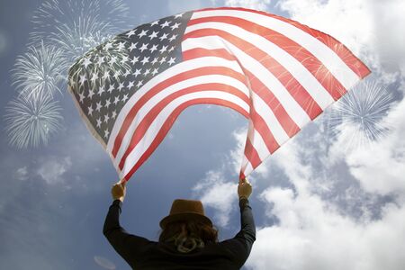Young happy patriot girl holding the american flag under the 4th of July fireworks.